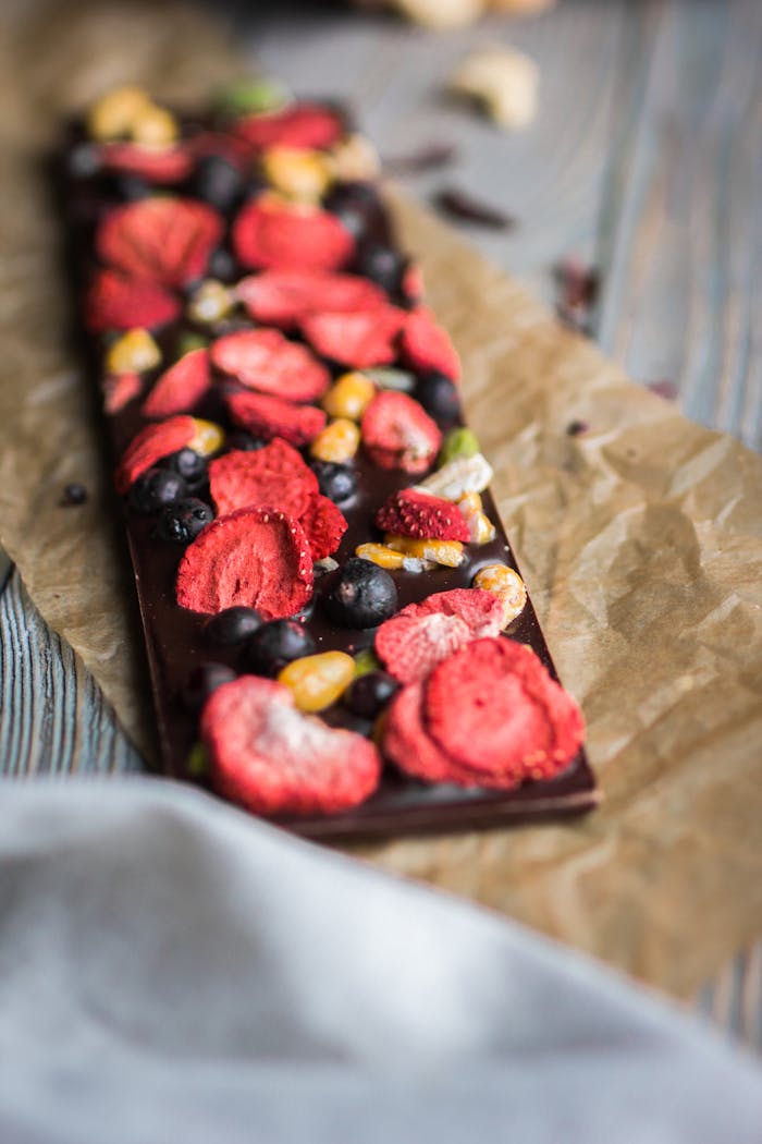Artistic chocolate bar topped with dried berries and nuts on parchment paper.