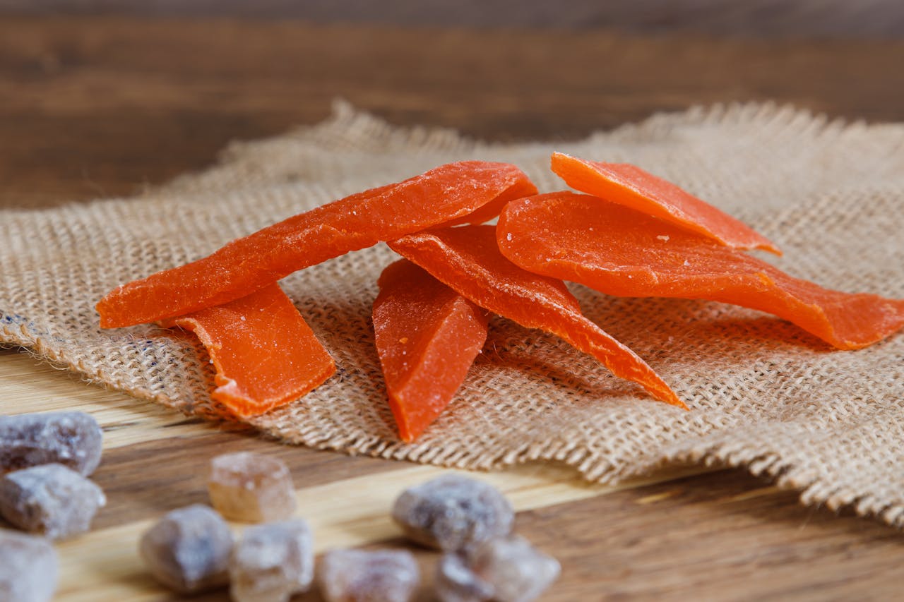 Close-up of dried papaya slices and candied ginger on a rustic burlap fabric.